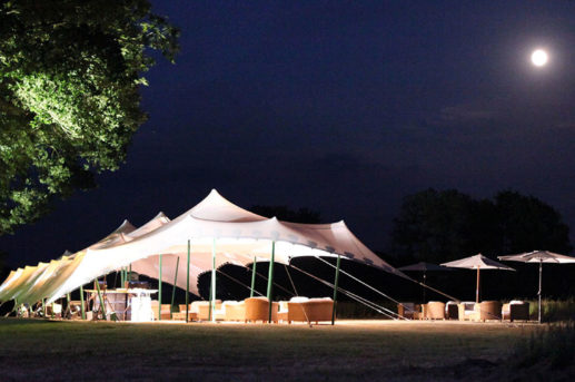 White stretch tent by moonlight, up lit trees.